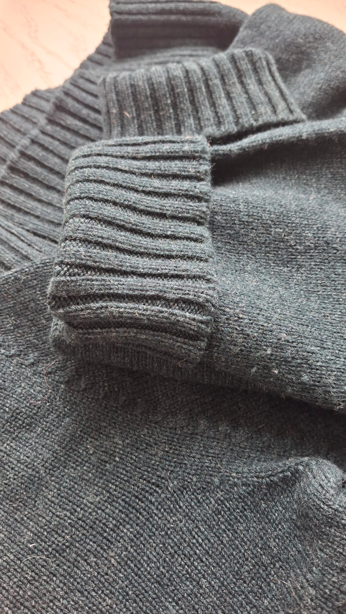 Close-up of a worn knitted cuff showing pilling, ready for repair